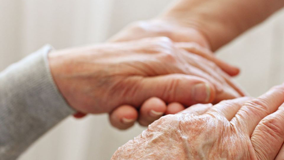 Zwei Handpaare, eines älter, dass andere jünger, fassen sich an.
