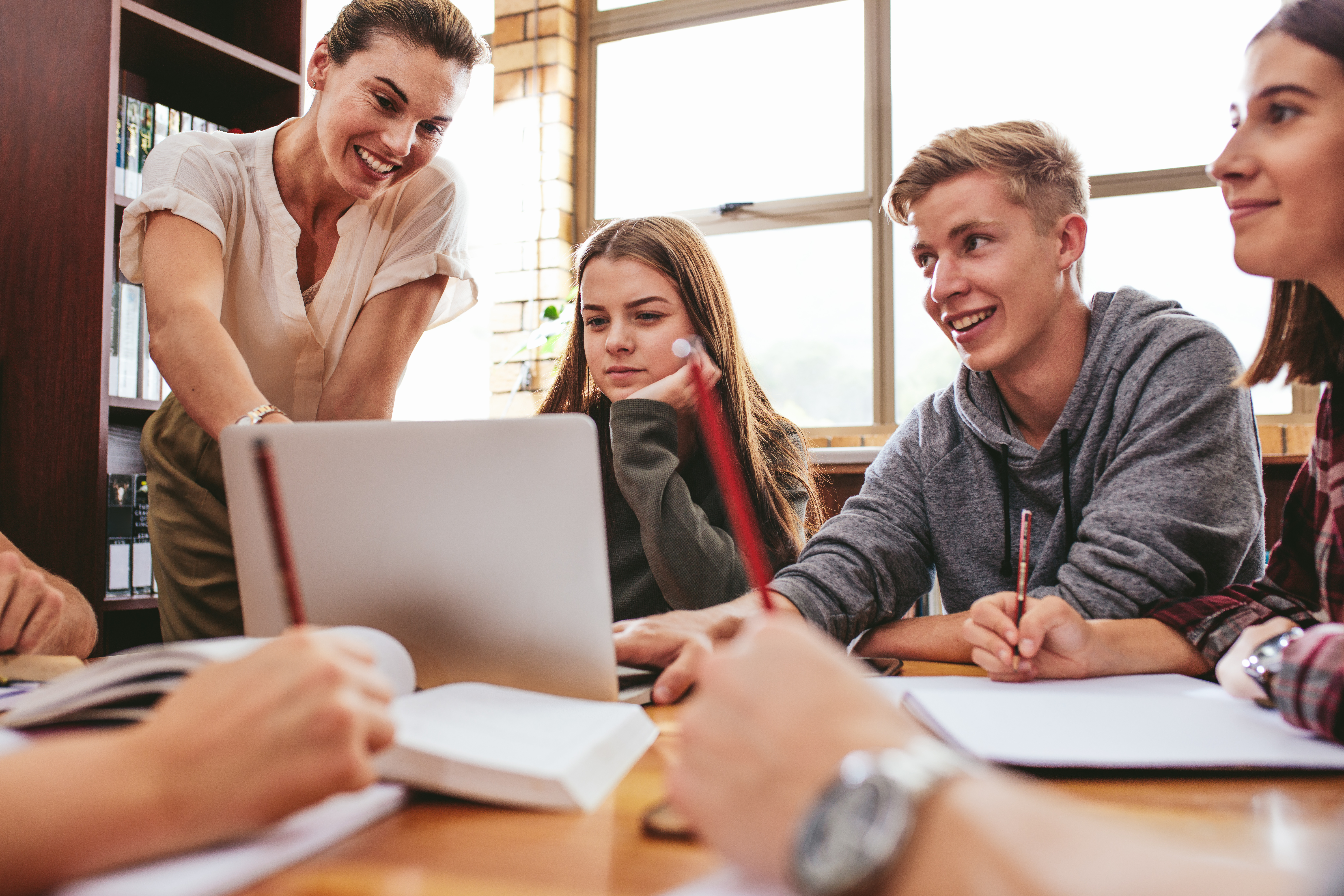 Eine Lehrerin erklärt zwei Studentinnen und einem Studenten etwas an einem Laptop.