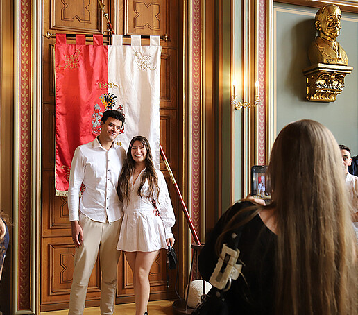 Eine Absolventin und ihre Begleitung machen ein Foto vor der Zittauer Fahne.