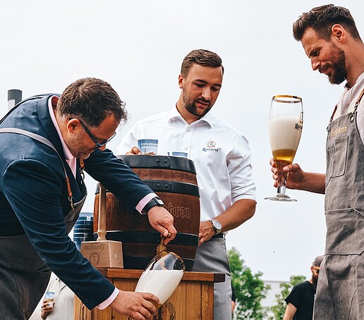 Der Rektor gießt ein Bierglas aus dem Bierfass mit Bier ein.