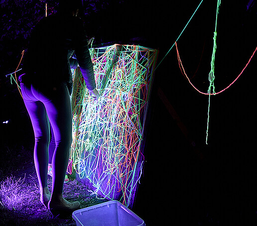 Eine Frau spannt neonleuchtende Farben über einen Rahmen.