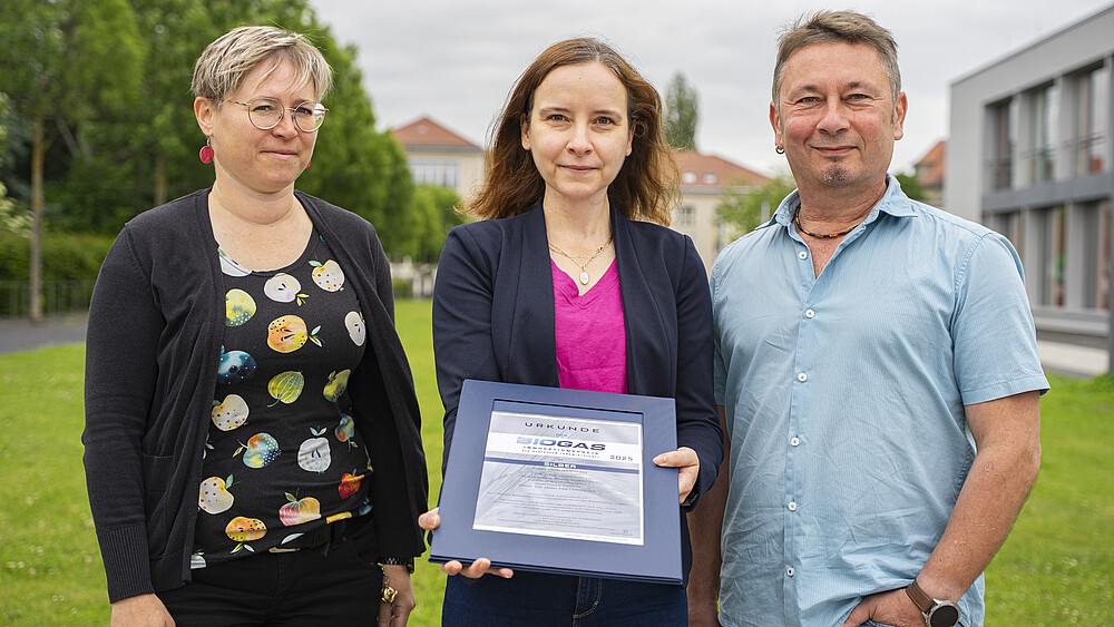 Frau Dr. Marzena Poraj-Kobielska, Frau Dr. Judit Harsányi und Herr Dipl.-Ing. Matthias Tirsch stehen auf einer Wiese auf der Zittauer Campusachse. Frau Dr. Harsanyi hält die Urkunde in den Händen.