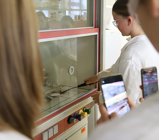 Eine Schülerin zündet eine Substanz in einem Schälchen unter dem Dunstabzug an.