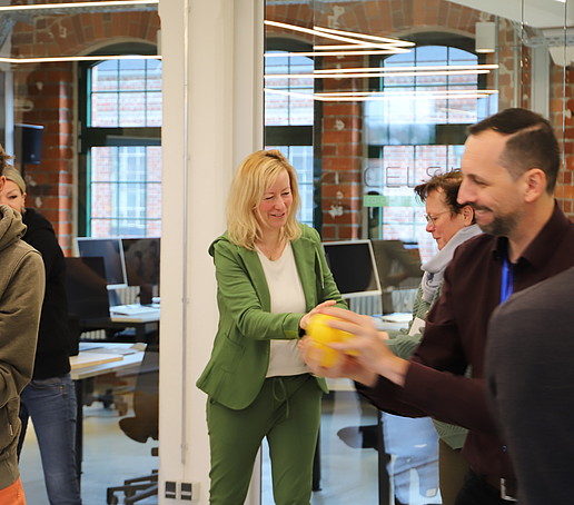 In einem großen Raum reichen sich Workshopteilnehmende einen orangenen Ball weiter.