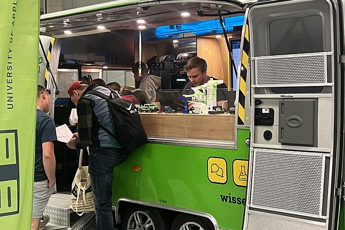 Im Bus finden Experimente statt. Besucher warten in einer Schlange.