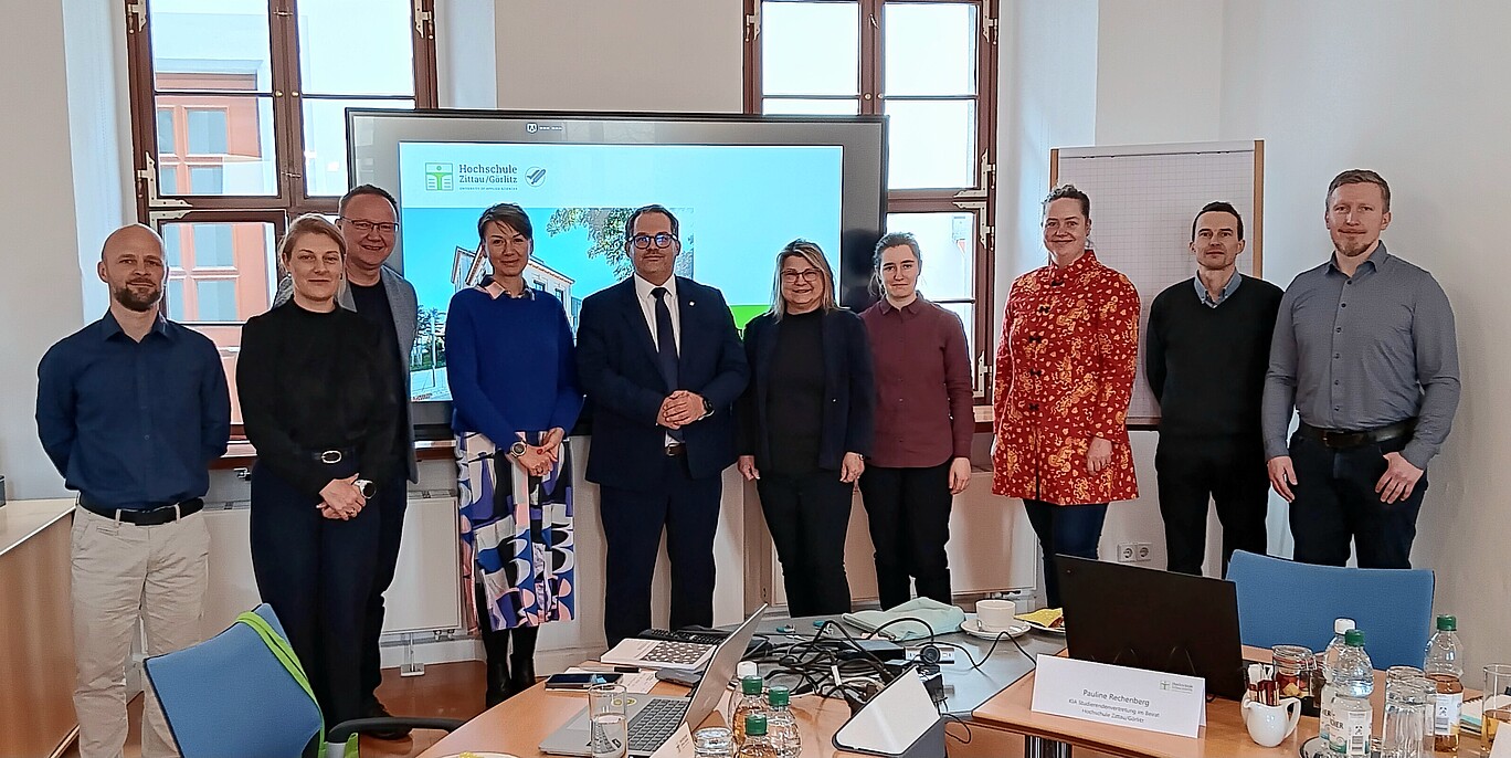 KIA-Beirat steht für ein Gruppenbild nebeneinander. Im Hintergrund steht ein Bildschirm.