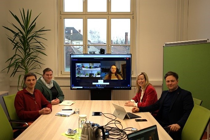 Im Seminarraum sitzen Studierende und die Prorektorin sowie Herr Winkler. Auf einem Monitor im Hintergrund ist jemand zum Gespräch zugeschaltet.