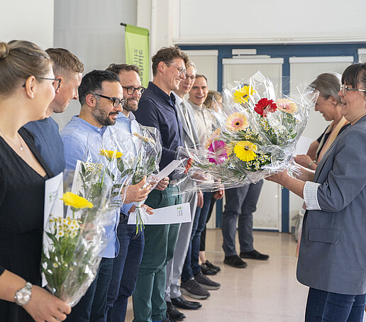 Eine Mitarbeiterin überreicht Kursabsolventinnen und Kursabsolventen einen Blumenstrauß.