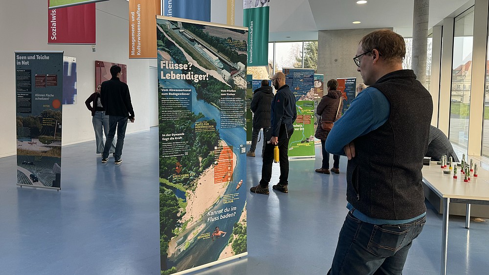 Ein Besucher steht vor einem Roll-up im Foyer von Haus Z Vier, umgeben von anderen Besuchenden der Ausstellung.