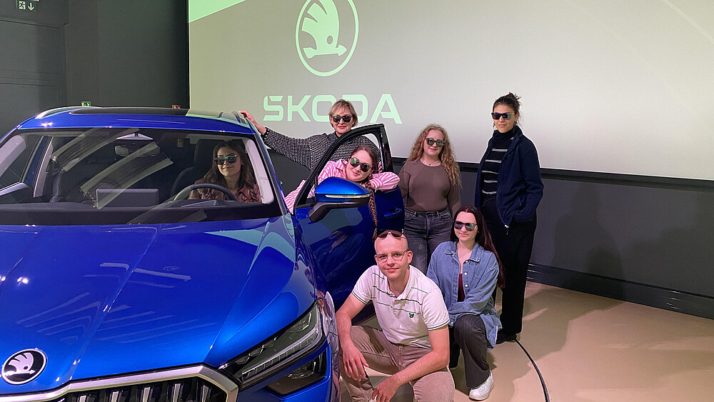 Mehrere Studierende stehen und hocken neben einem blauen Skoda.