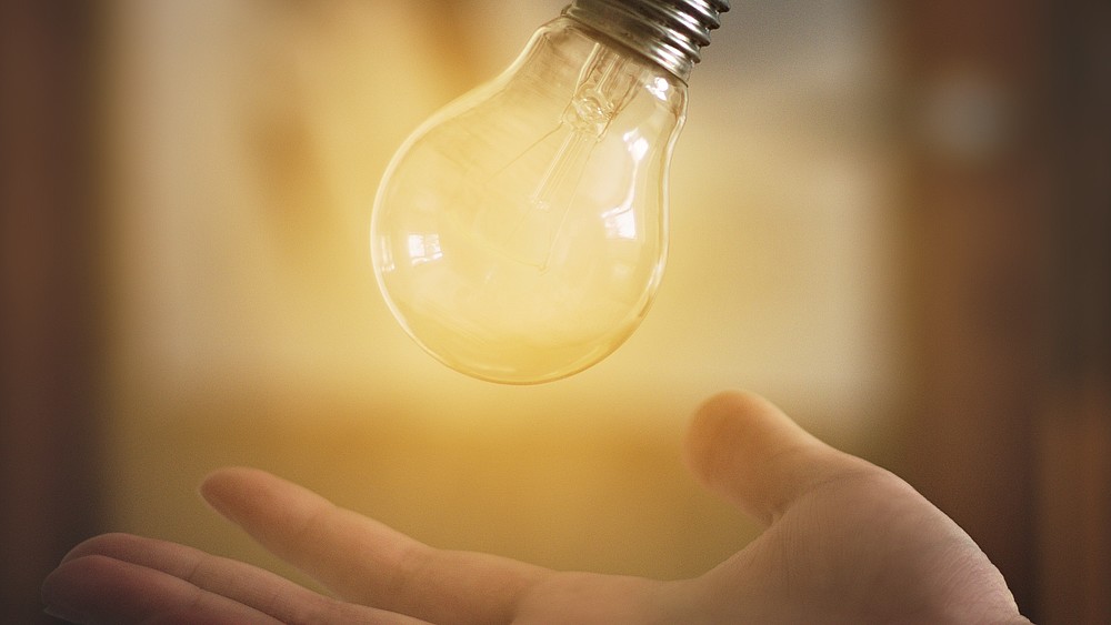 Über einer offenen Hand schwebt eine Glühbirne. Sie wird von hinten hell erleuchtet.