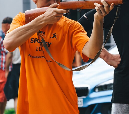 Ein Student hält ein Gewähr im Arm und legt an.