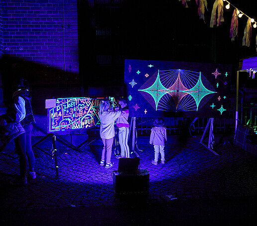 Kinder malen mit Neonfarben auf einer Leinwand.