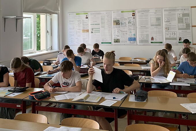 Schülerinnen und Schüler sitzen im Seminarraum an Tischen und arbeiten mit Prüfungsunterlagen.