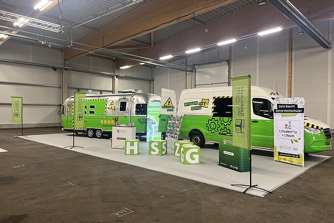 Vor Messebeginn ist der komplette Stand in der Halle aufgebaut. Der Bus mit Anhänger, der Messestand mit Fahnen und Sitzwürfeln, Theken und Aufstellern.