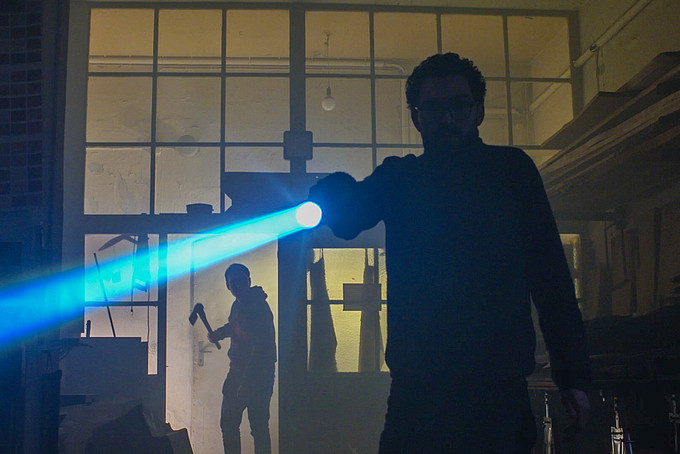 In einer dunklen Kulisse schwenkt ein Mann mit Brille eine Taschenlampe.