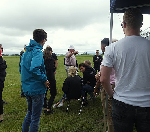 Studierende und Professoren stehen zusammen und besprechen den Ablauf. Einige machen Fotos.