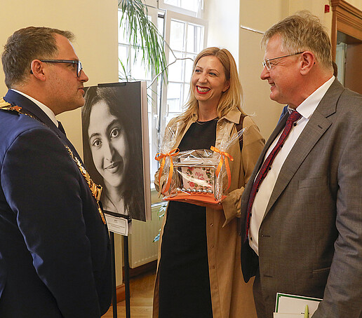 Der Rektor unterhält sich mit zwei Gästen, die ihm ein Geschenk überreichen.