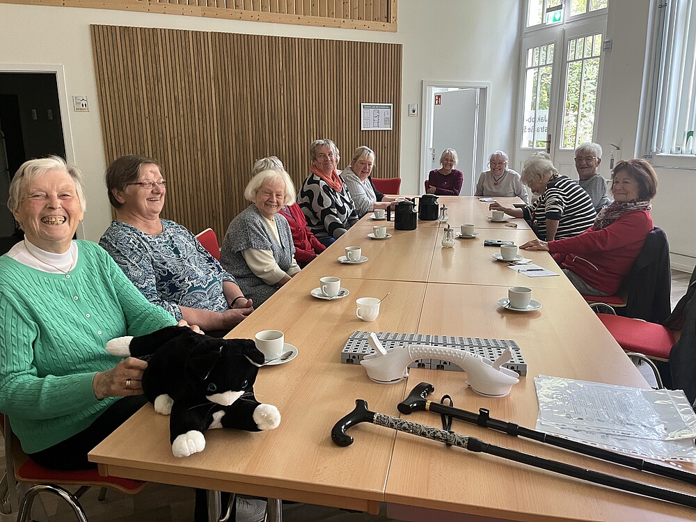 Viele ältere Damen sitzen um einen großen Tisch mit verschiedenen technischen Hilfsmitteln