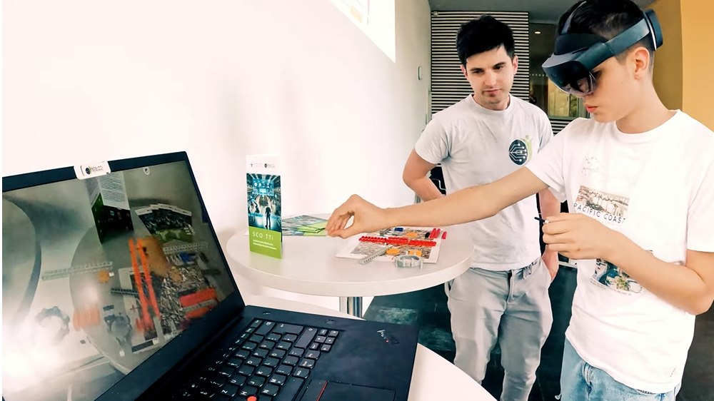 Der Schüler Henry trägt eine VR-Brille und streckt einen Arm aus. Er wird daneben von einem Mitarbeiter beobachtet.