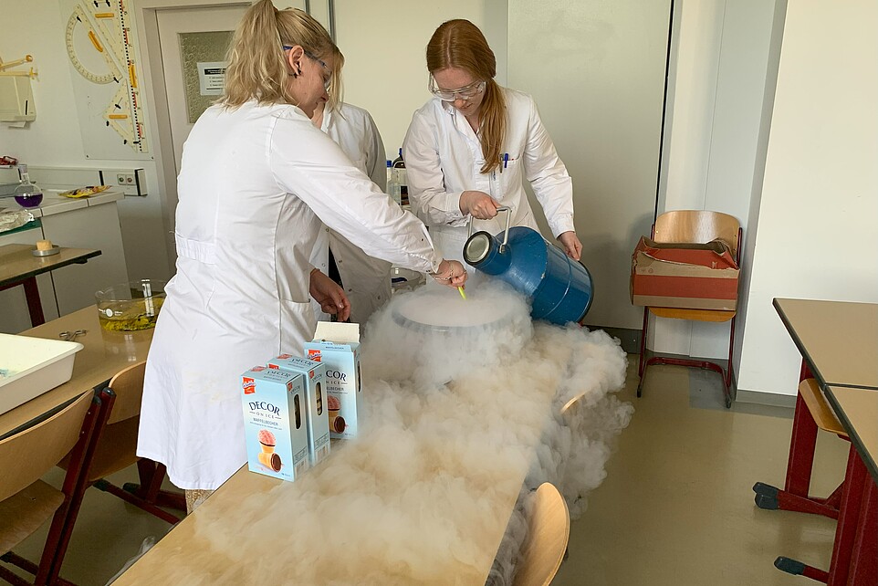 Eine Labormitarbeiterin und eine Schülerin stellen Eis her im Seminarraum.