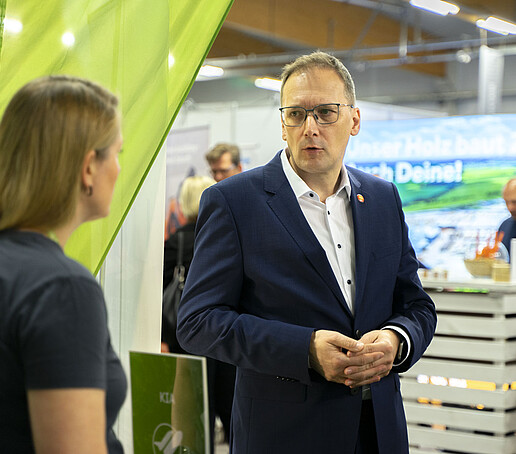 Ein Mann im Anzug unterhält sich mit der KIA-Beauftragten am KIA-Stand.