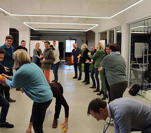 In einem großen Raum reichen sich Workshopteilnehmende einen orangenen Ball weiter.