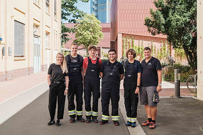 Auf dem Außengelände stehen zum Gruppenbild die KIA-Beauftragte, vier KIA-Studierende und ein Mitarbeiter nebeneinander und lächeln.