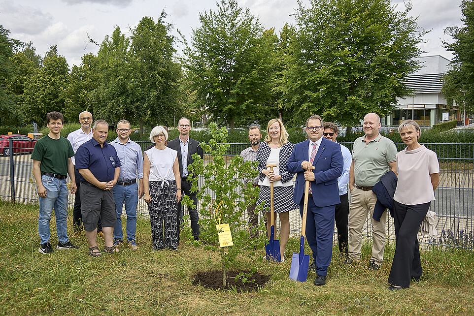 Die Hochschulleitung und Hochschulvertretende stehen teilweise mit Schaufeln um einen eingepflanzten Baum.