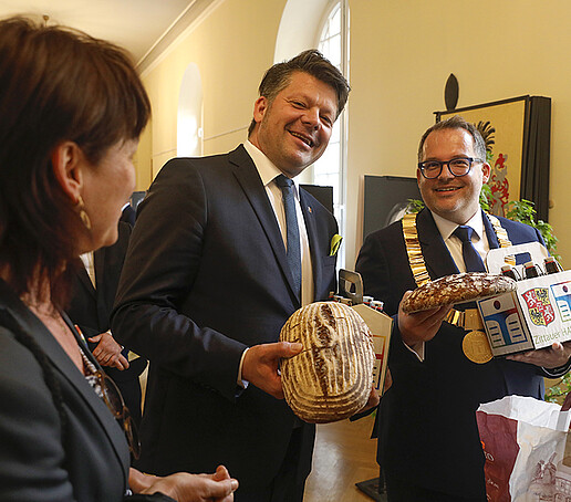 Der Rektor nimmt Geschenke von Herrn Zenker entgegen. Es sind zwei Brote und ein kleiner Kasten mit Bierflaschen. Auf dem Kasten steht: Zittauer HAW-Bräu.