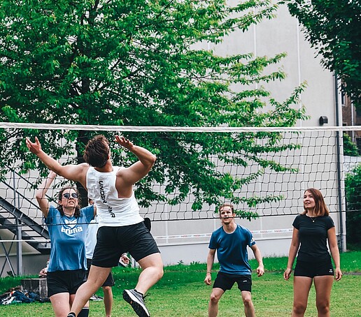 Eine Gruppe Studierender spielt Volleyball auf dem Rasen.