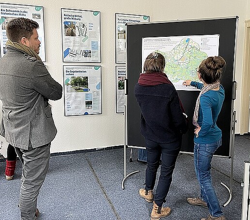 Zwei Interessierte schauen sich eine Stadtkarte an einem Ausstellungsboard an.