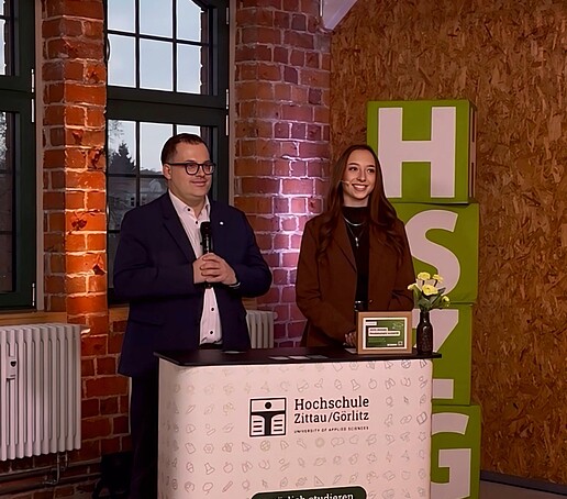 Der Rektor und die Moderatorin stehen hinter der Messetheke im TV-Studio.