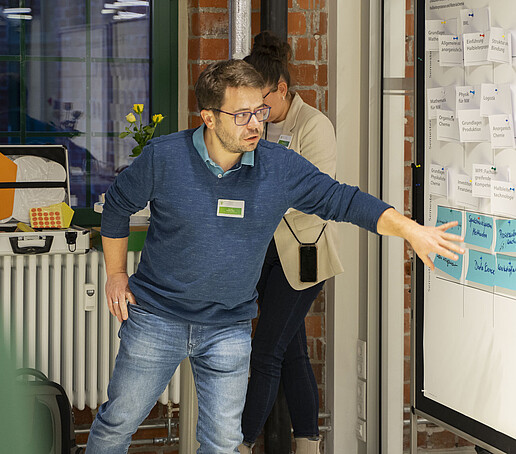 Ein Teilnehmender führt etwas aus mit Hilfe der Zettel, die an einem Whiteboard angebracht sind.
