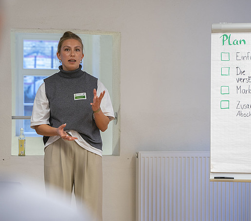 Eine Teilnehmerin steht neben einem Flipchart und erklärt dem Publikum etwas.