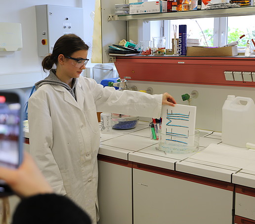 Eine Schülerin hält ein Styroporschild in eine Schale voll Flüssigkeit.