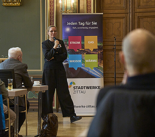 Eine Teilnehmerin steht vor einem Roll-up und richtet Worte an das Publikum.