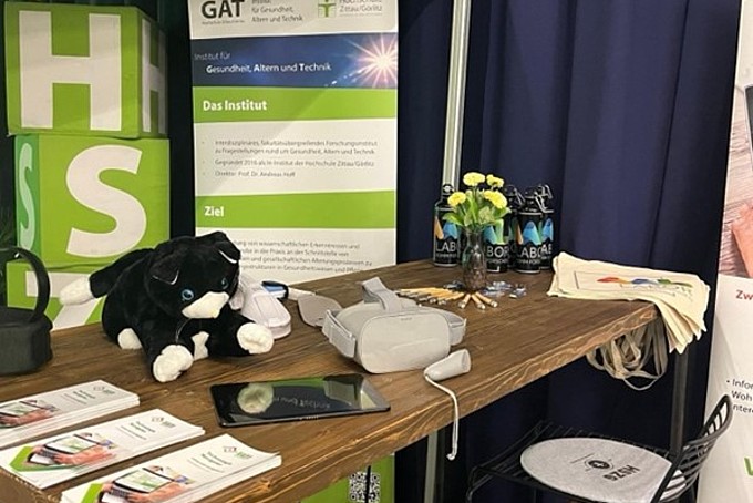 Der Infostand des GAT-Instituts mit ausgelegten Flyern und der Plüschkatze sowie Blumen und technischen Geräten.
