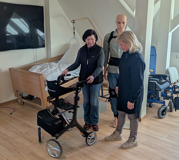 2 Frauen stehen nebeneinander. Eine davon fährt mit einem Rollator