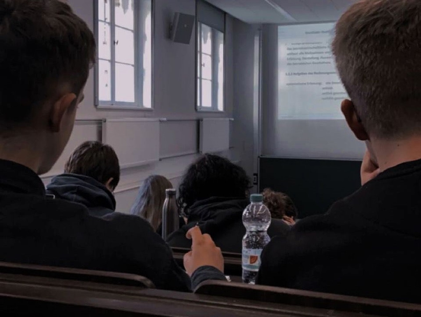 Im Hörsaal, Blick aus den Bankreihen auf die Leinwand.