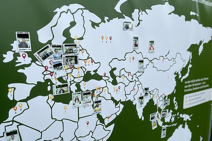 Auf einer Weltkarte sind Polaroid-Fotos angepinnt.