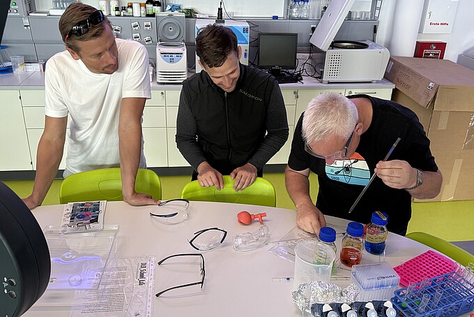 Drei Lehrer beugen sich über einen Versuchsstand.
