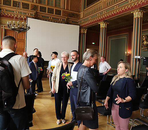 Ein Absolvent macht mit Frau Leuschner ein Erinnerungsfoto. Daneben unterhält sich die Prorektorin mit einer Dozentin.