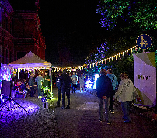 Der StuRa-Stand mit Roll-up und Pavillion und einer Lichterkette, Besucher laufen daran vorbei.