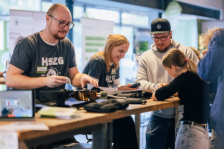 2 Mitarbeiter am Messestand erklären 2 Besuchern ein Gerät