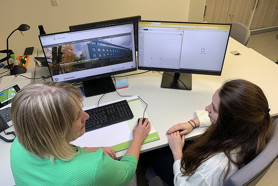 Kerstin Korb und Maren Molch sitzen am Schreibtisch vor dem PC-Bildschirm und sprechen miteinander.