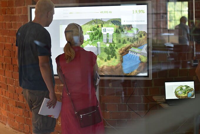 Besuchende schauen sich eine Präsentation auf einem digitalen Bildschirm an.