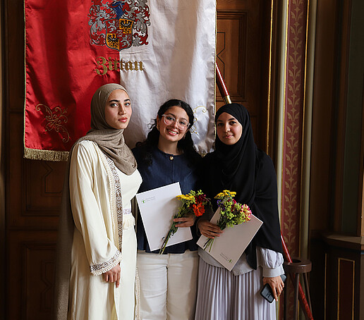 Drei Absolventinnen machen vor der Zittauer Fahne ein Erinnerungsfoto.