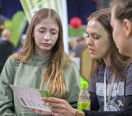 Eine Studieninteressierte bespricht einen Flyer mit einer studentischen Hilfskraft.