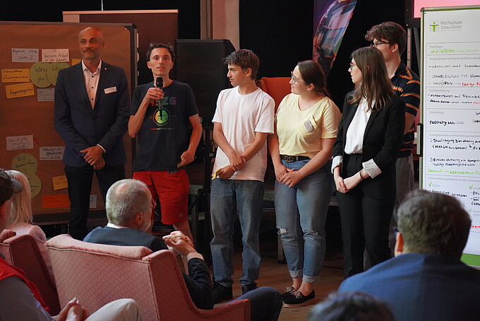 Teilnehmende präsentieren ihre Ideen auf der Bühne vor einem Publikum.